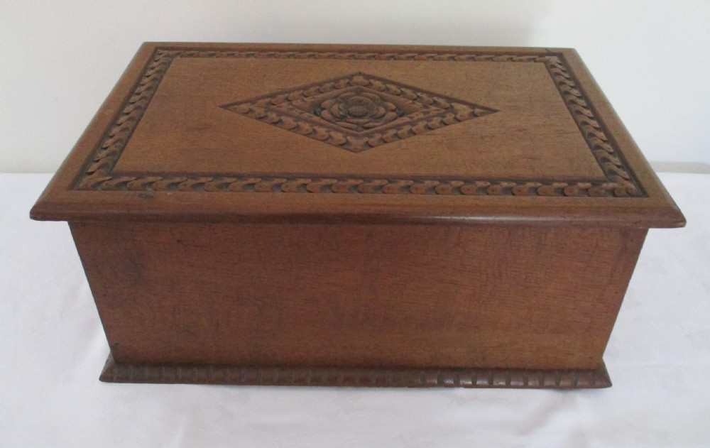 A rectangular carved oak box featuring a flat hinged lid with a carved central lozenge motif, carved borders, and a dark iron lock plate on the front panel. View IV