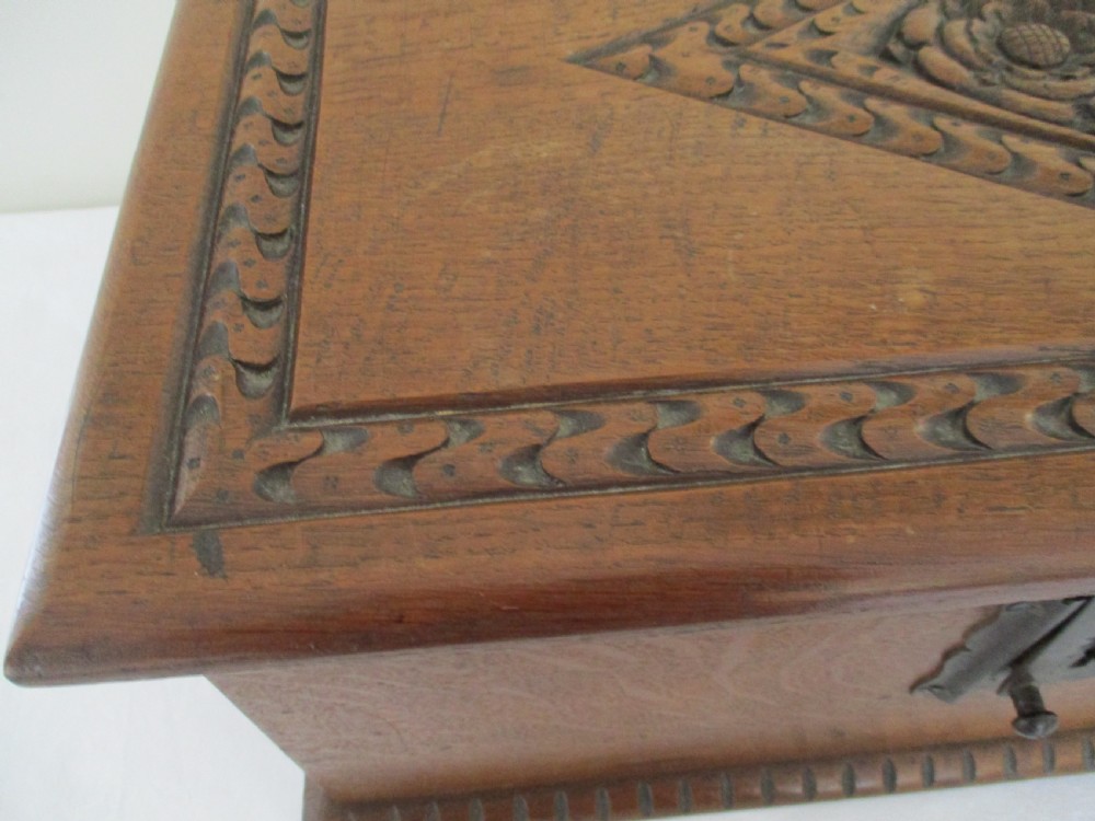 A rectangular carved oak box featuring a flat hinged lid with a carved central lozenge motif, carved borders, and a dark iron lock plate on the front panel. View IX