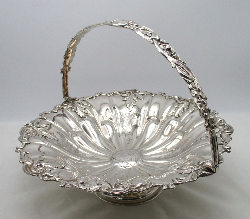 A 19th-century silver-plated bread basket featuring a fluted rim, floral engraving, pedestal base, and an arched swing handle.