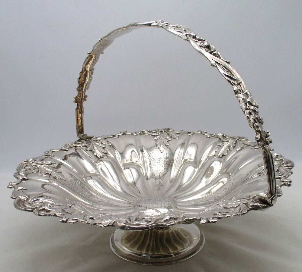 A 19th-century silver-plated bread basket featuring a fluted rim, floral engraving, pedestal base, and an arched swing handle. View II
