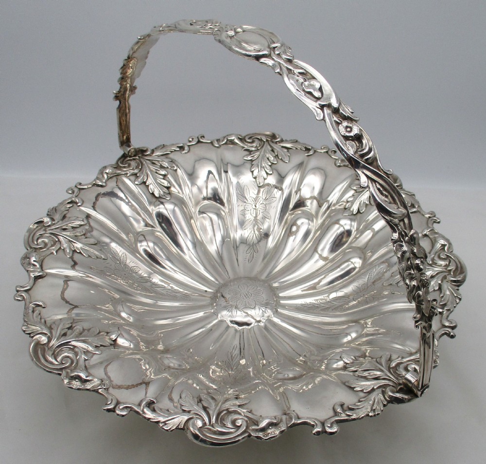 A 19th-century silver-plated bread basket featuring a fluted rim, floral engraving, pedestal base, and an arched swing handle. View III