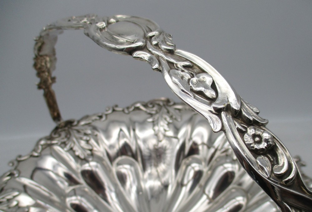 A 19th-century silver-plated bread basket featuring a fluted rim, floral engraving, pedestal base, and an arched swing handle. View V