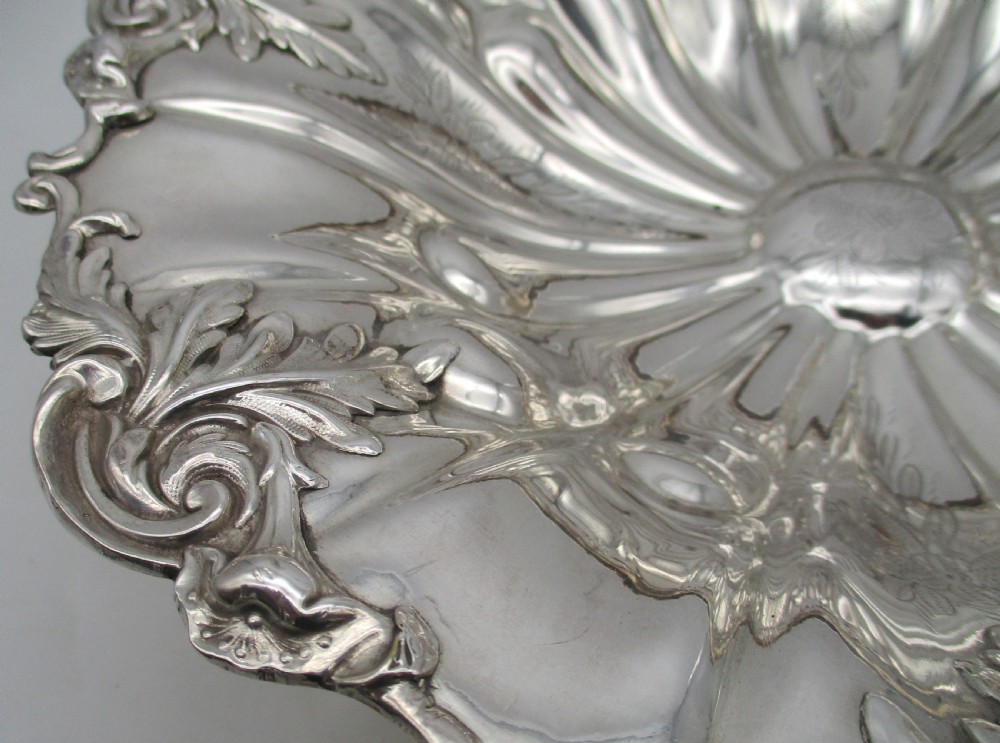 A 19th-century silver-plated bread basket featuring a fluted rim, floral engraving, pedestal base, and an arched swing handle. View VI