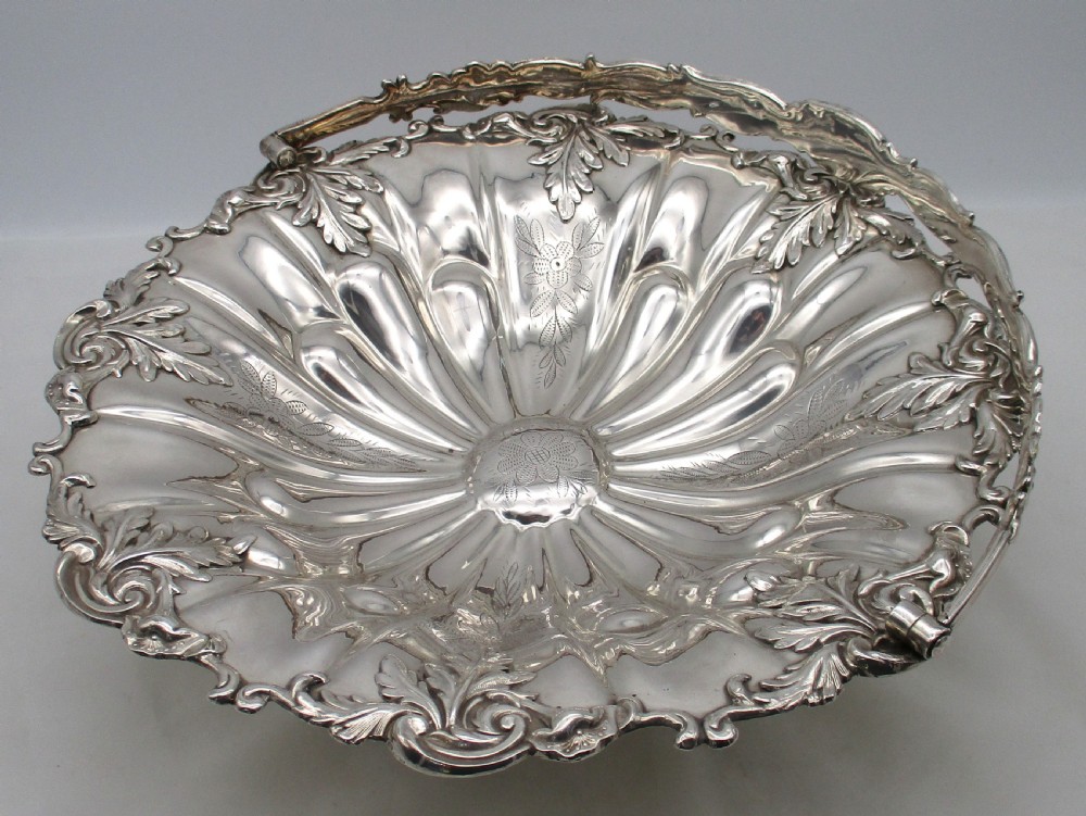 A 19th-century silver-plated bread basket featuring a fluted rim, floral engraving, pedestal base, and an arched swing handle. View VII