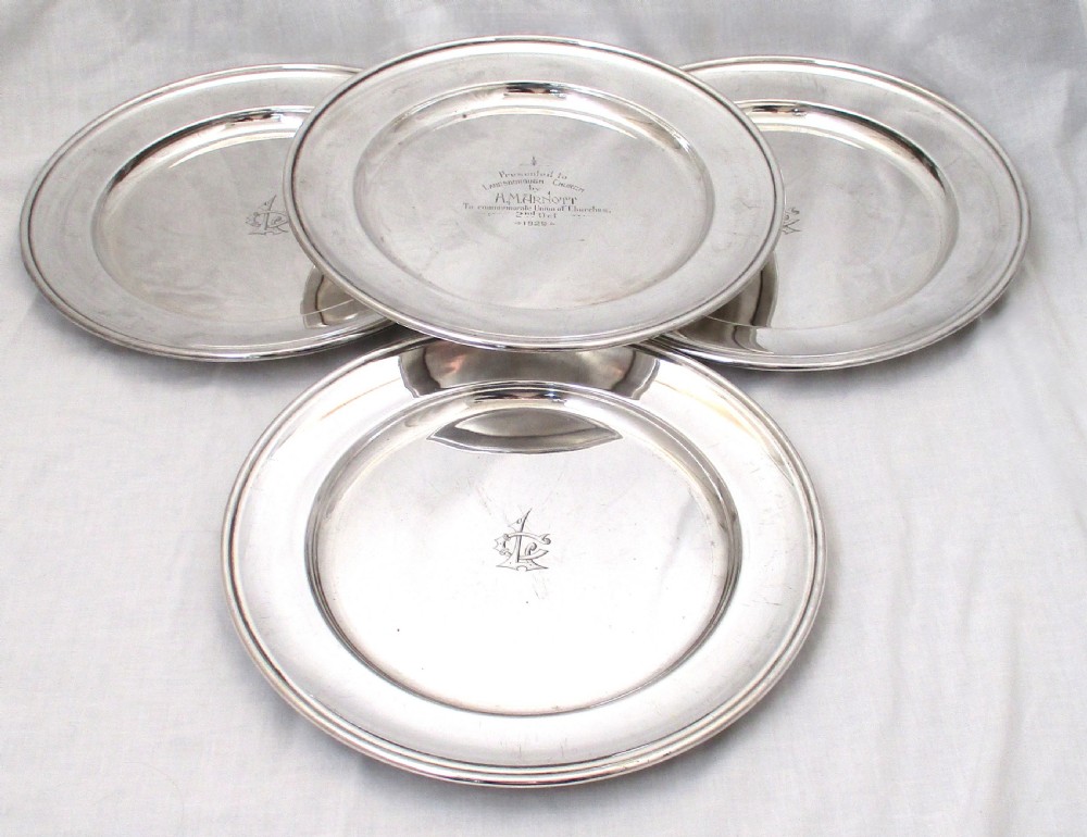 A set of four circular silver plated charger plates featuring wide flat rims and engraved central inscriptions and monograms.