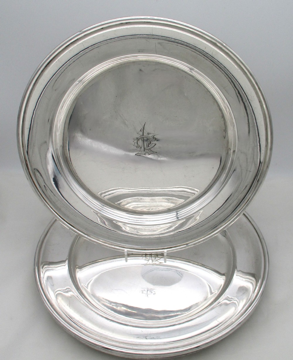 A set of four circular silver plated charger plates featuring wide flat rims and engraved central inscriptions and monograms. View II