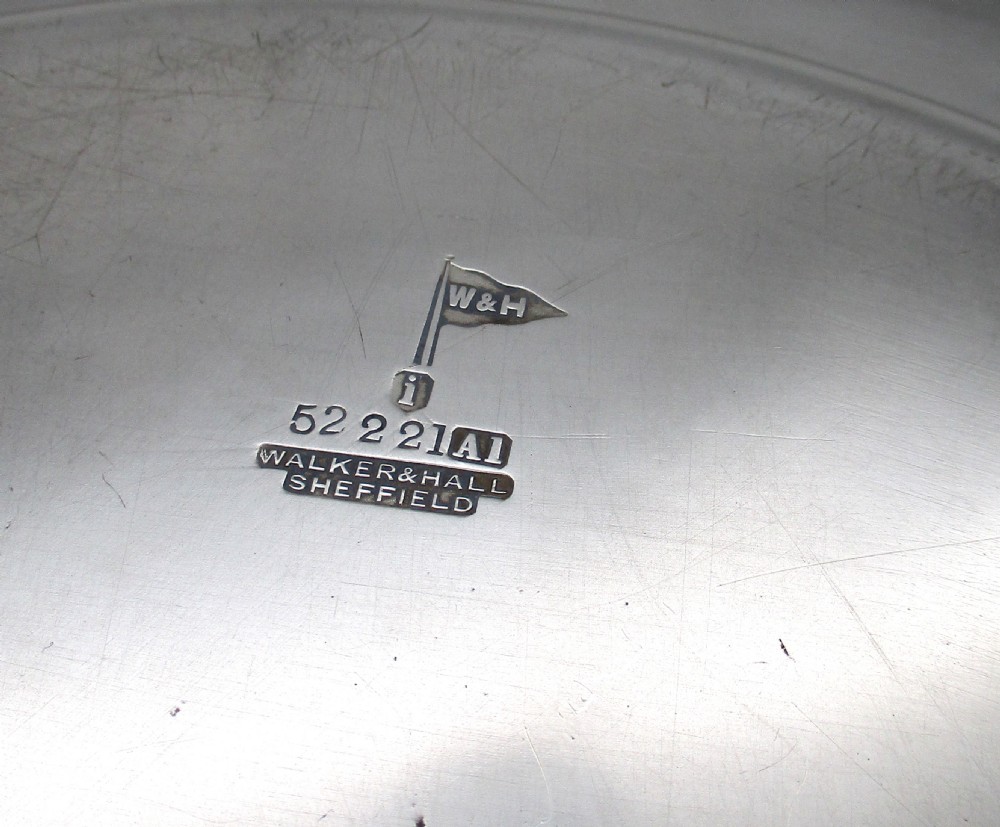 A set of four circular silver plated charger plates featuring wide flat rims and engraved central inscriptions and monograms. View VII