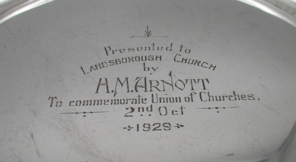 A set of four circular silver plated charger plates featuring wide flat rims and engraved central inscriptions and monograms. View VIII