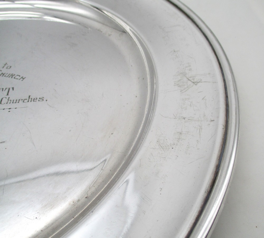 A set of four circular silver plated charger plates featuring wide flat rims and engraved central inscriptions and monograms. View IX