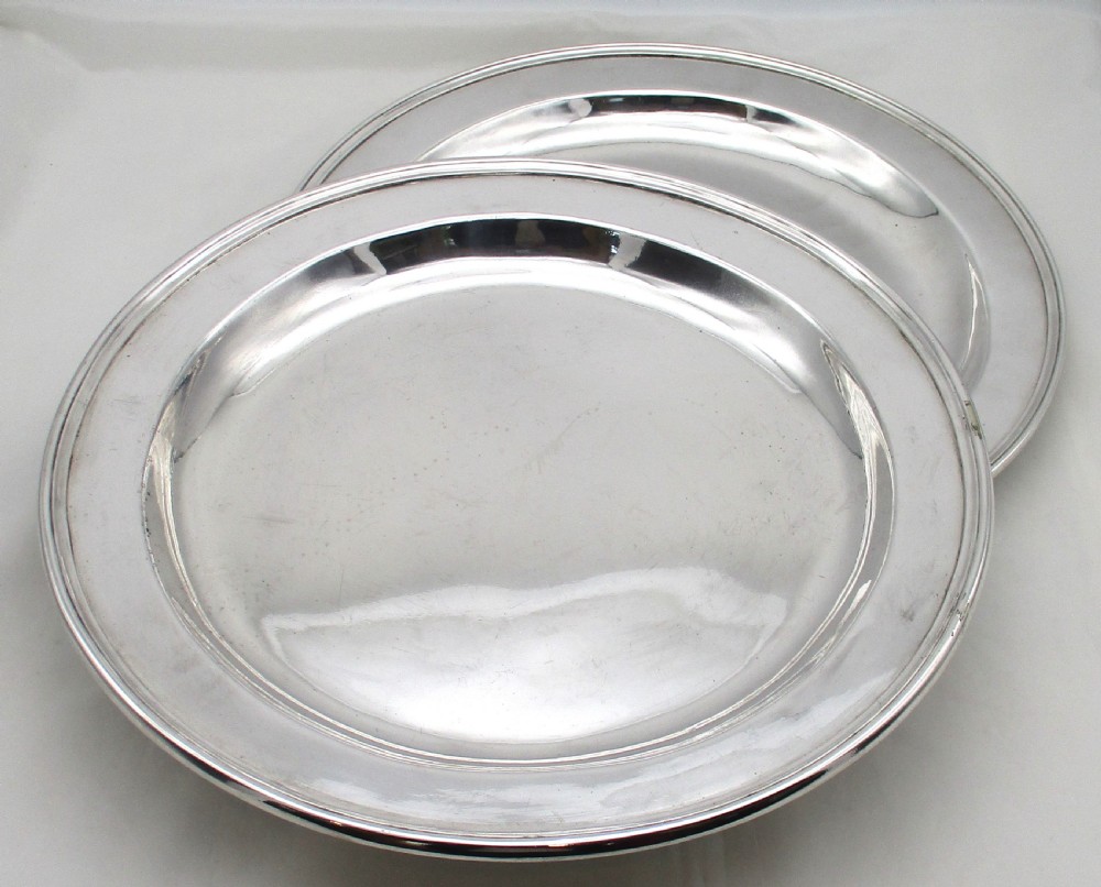 A pair of circular 14-inch silver-plated charger plates with polished central wells and simple reeded rims.