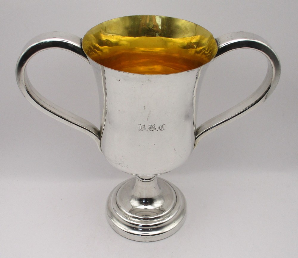A 19th-century silver-plated two-handled loving cup with a gilt interior and central monogram engraving on a stepped circular pedestal base.