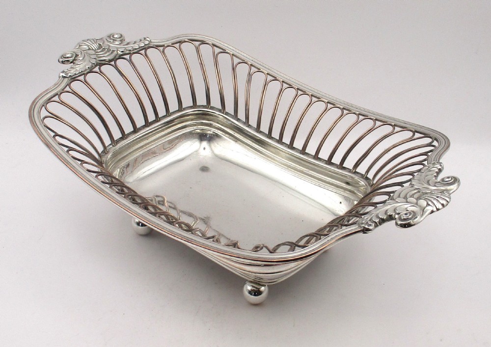 An antique Georgian Old Sheffield silver-plated wirework basket featuring flaring side wires, shell motif handles, and ball feet.