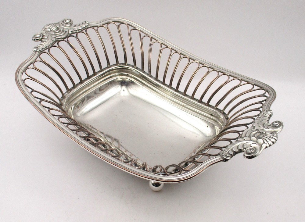 An antique Georgian Old Sheffield silver-plated wirework basket featuring flaring side wires, shell motif handles, and ball feet. View II
