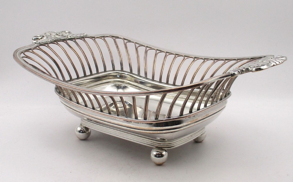 An antique Georgian Old Sheffield silver-plated wirework basket featuring flaring side wires, shell motif handles, and ball feet. View III
