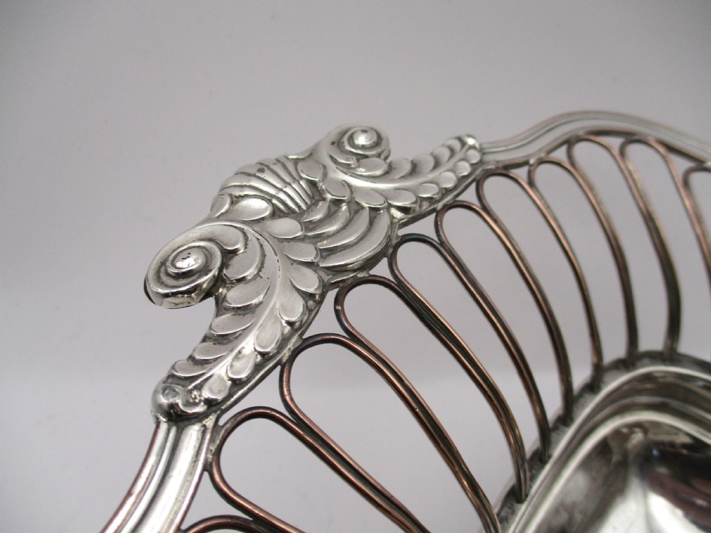 An antique Georgian Old Sheffield silver-plated wirework basket featuring flaring side wires, shell motif handles, and ball feet. View IV