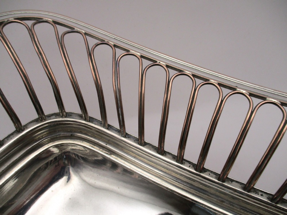 An antique Georgian Old Sheffield silver-plated wirework basket featuring flaring side wires, shell motif handles, and ball feet. View V