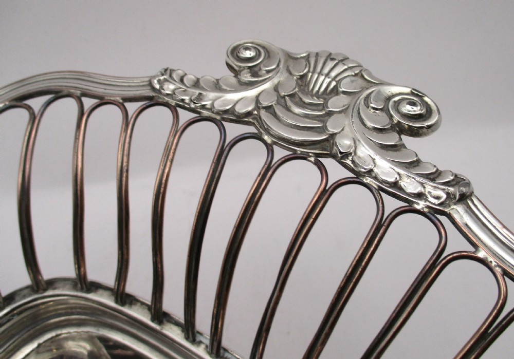 An antique Georgian Old Sheffield silver-plated wirework basket featuring flaring side wires, shell motif handles, and ball feet. View VI