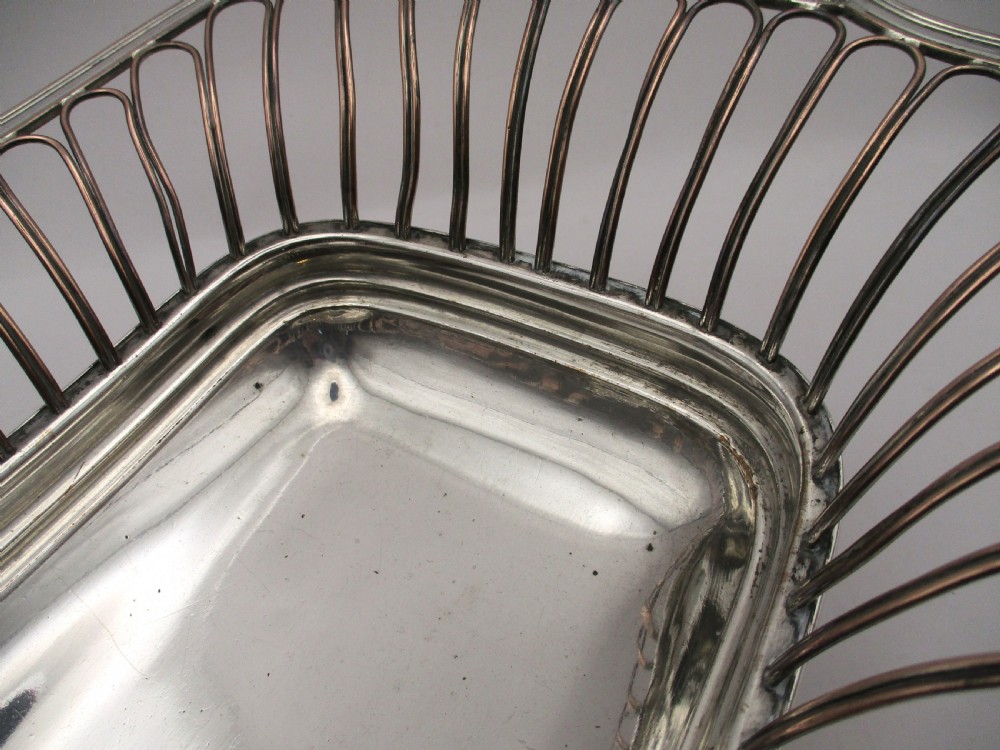 An antique Georgian Old Sheffield silver-plated wirework basket featuring flaring side wires, shell motif handles, and ball feet. View VII