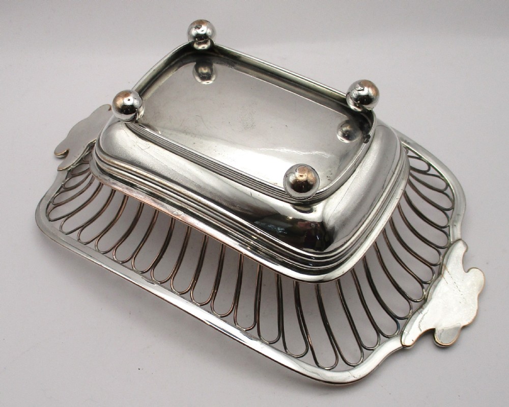 An antique Georgian Old Sheffield silver-plated wirework basket featuring flaring side wires, shell motif handles, and ball feet. View VIII