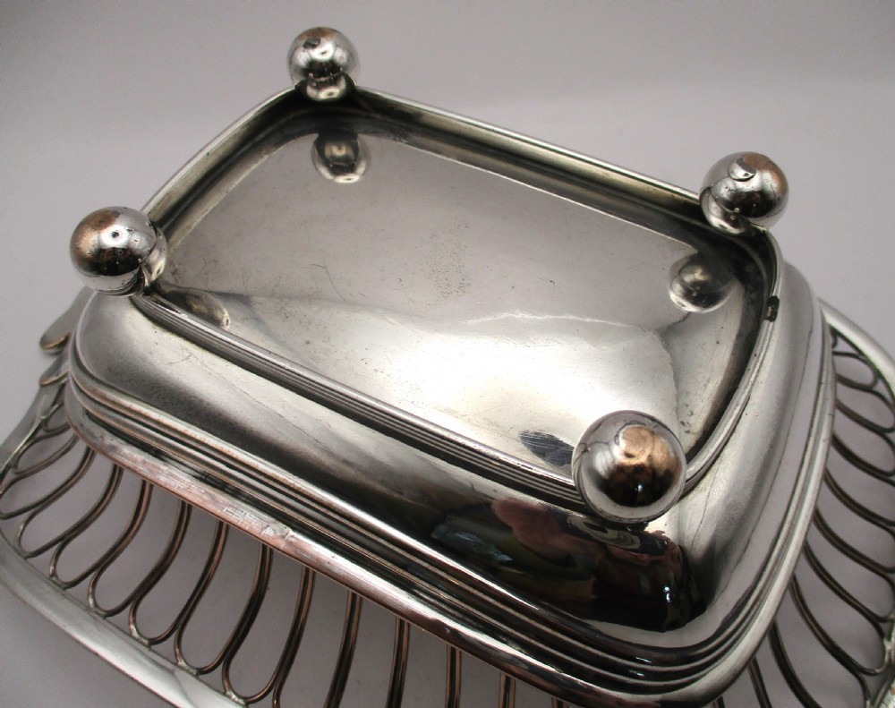 An antique Georgian Old Sheffield silver-plated wirework basket featuring flaring side wires, shell motif handles, and ball feet. View IX
