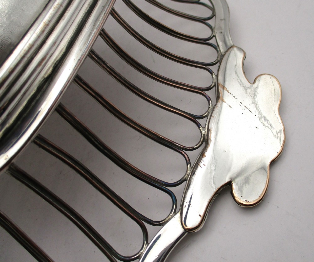 An antique Georgian Old Sheffield silver-plated wirework basket featuring flaring side wires, shell motif handles, and ball feet. View X