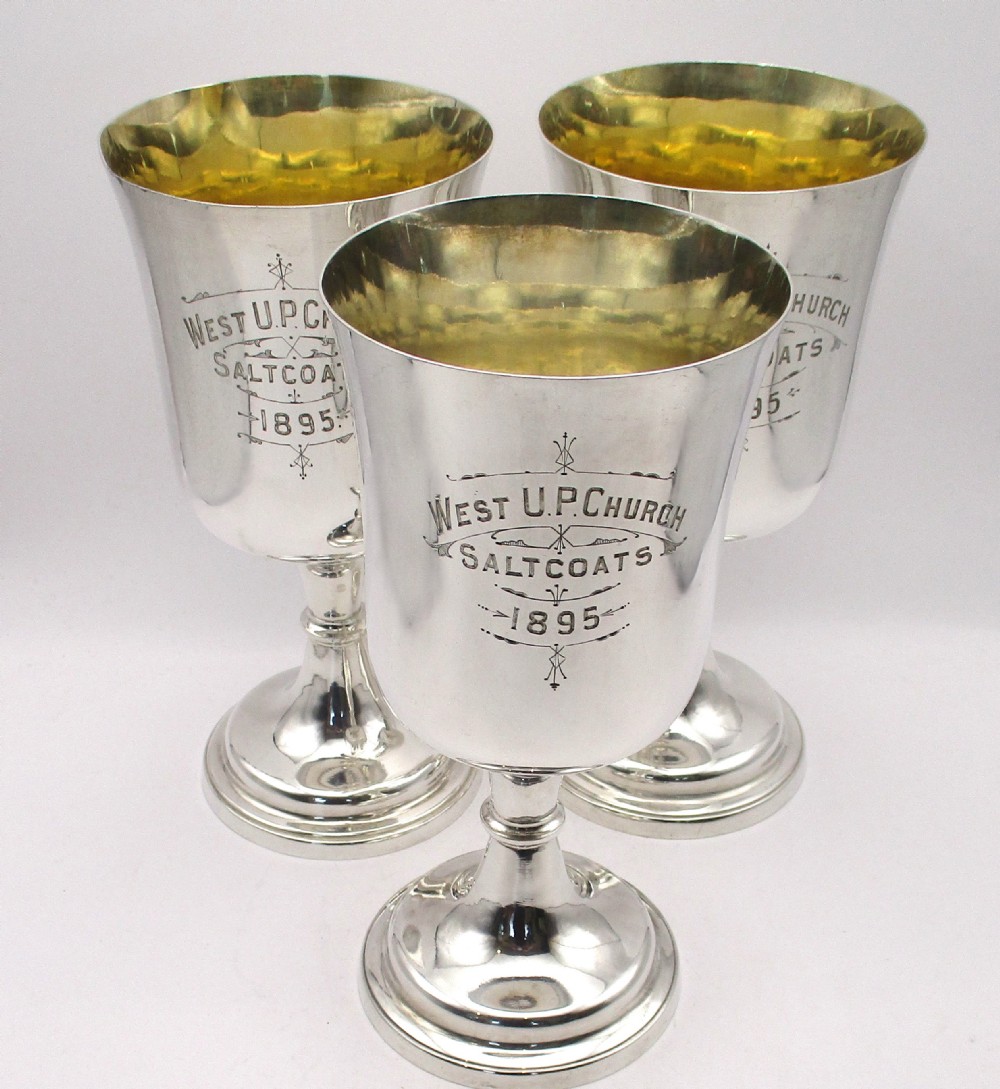 A set of three silver-plated chalices featuring engraved inscriptions on the exterior and gilded interiors on turned pedestal bases.