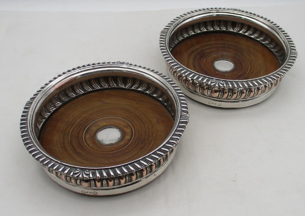 A pair of Georgian Old Sheffield Plated wine coasters featuring turned wooden bases with silver central bosses and gadrooned metal rims.