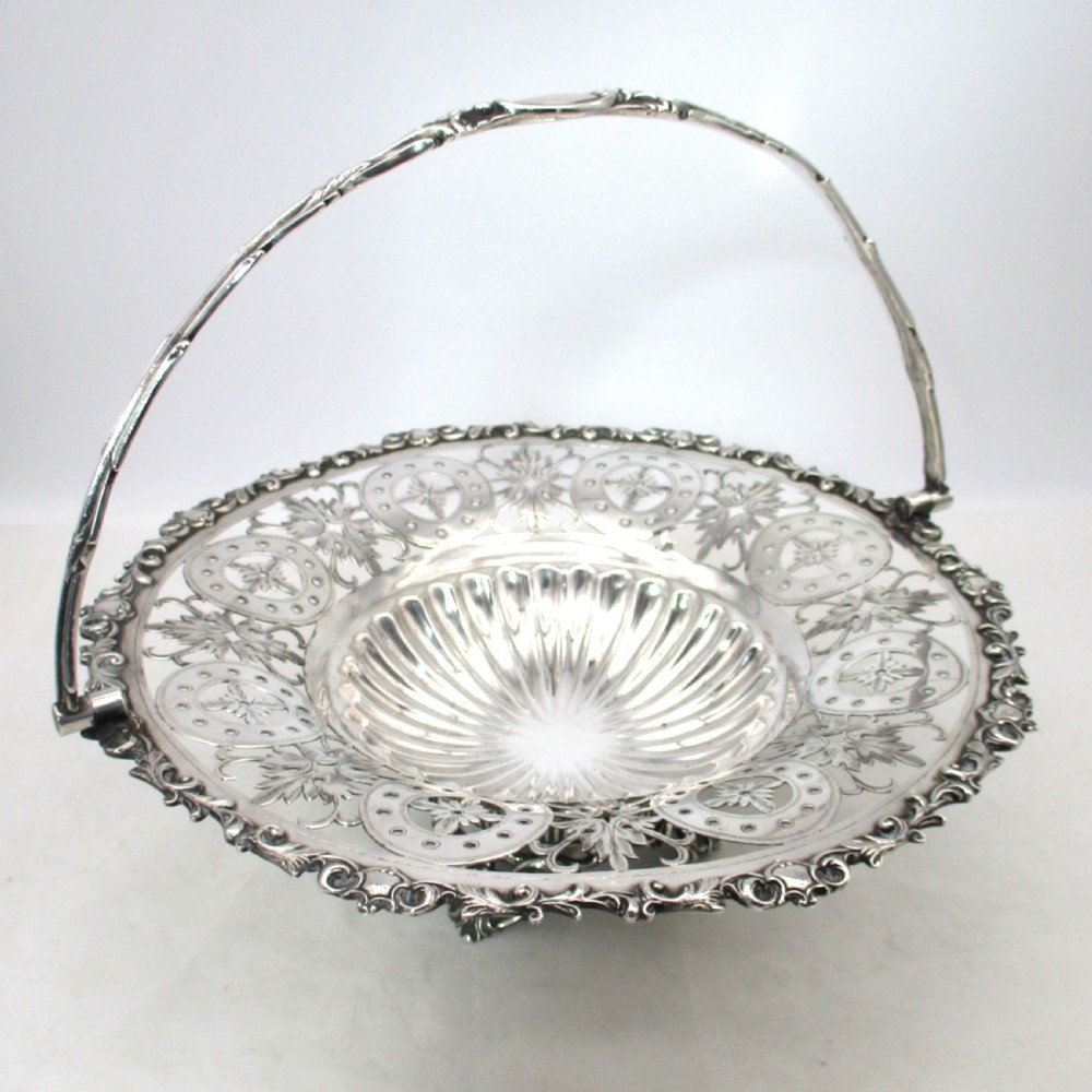 A nineteenth-century circular silver-plated cake basket featuring an arched swing handle, pierced foliate border, and fluted dish.