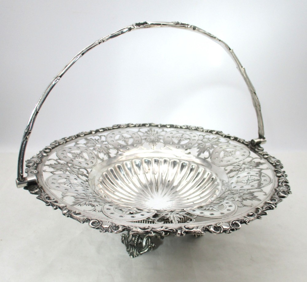 A nineteenth-century circular silver-plated cake basket featuring an arched swing handle, pierced foliate border, and fluted dish. View II