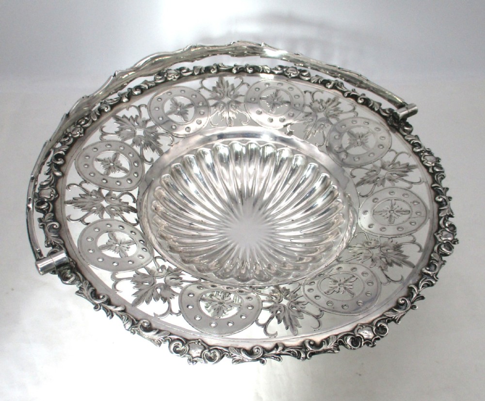 A nineteenth-century circular silver-plated cake basket featuring an arched swing handle, pierced foliate border, and fluted dish. View IV