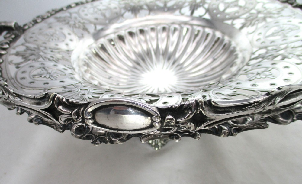 A nineteenth-century circular silver-plated cake basket featuring an arched swing handle, pierced foliate border, and fluted dish. View V