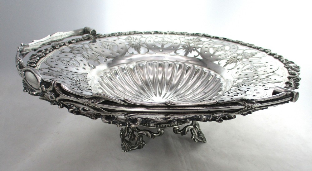 A nineteenth-century circular silver-plated cake basket featuring an arched swing handle, pierced foliate border, and fluted dish. View VI