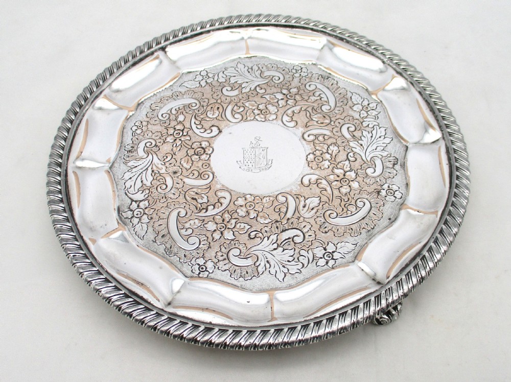 A circular Regency period Old Sheffield plated card tray featuring an engraved floral surface, armorial crest centre, pie-crust rim, and rope-twist border.
