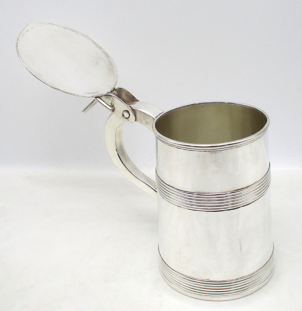 A silver-plated lidded tankard featuring a hinged lid with a thumbpiece, horizontal reeded banding, and a glass base. View VI