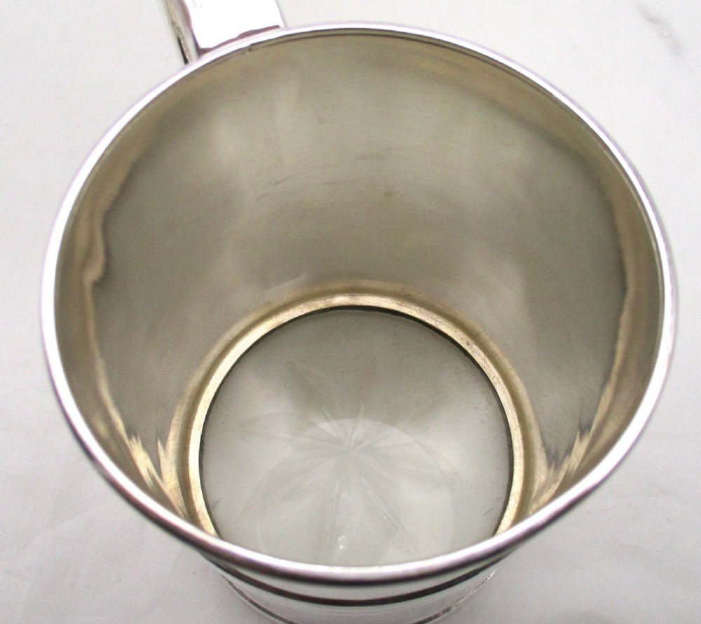 A silver-plated lidded tankard featuring a hinged lid with a thumbpiece, horizontal reeded banding, and a glass base. View VII