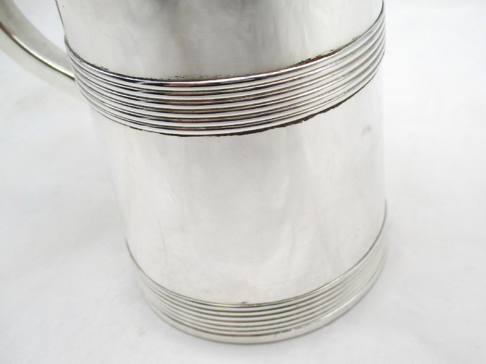 A silver-plated lidded tankard featuring a hinged lid with a thumbpiece, horizontal reeded banding, and a glass base. View X