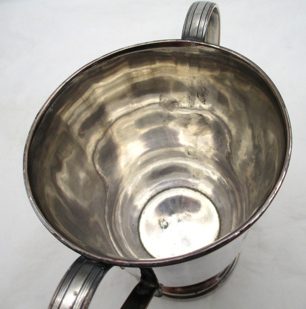 A Georgian silver-plated two-handled cup featuring a flared pedestal foot, looped side handles, and a central engraved crest. View IV