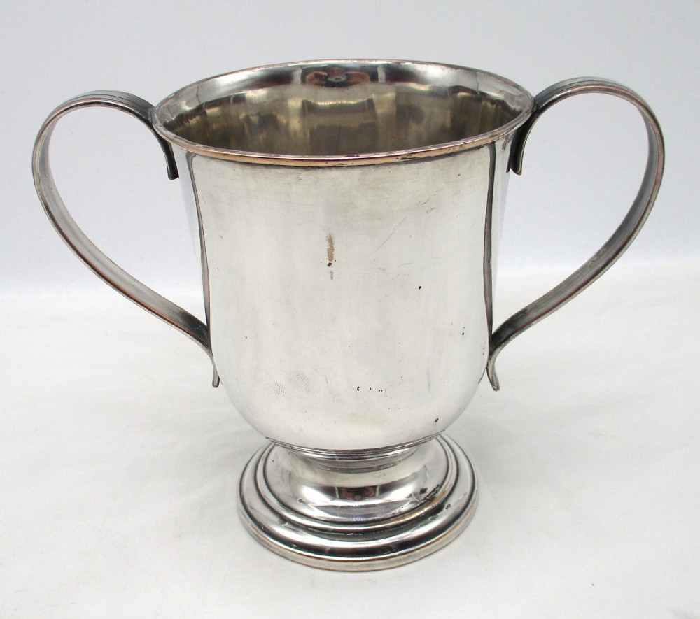A Georgian silver-plated two-handled cup featuring a flared pedestal foot, looped side handles, and a central engraved crest. View V