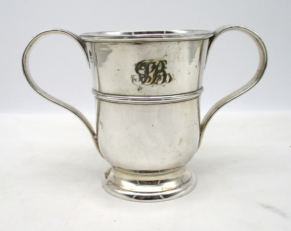 An antique silver-plated two-handled loving cup featuring a central girdle band, moulded foot, and an engraved monogram.