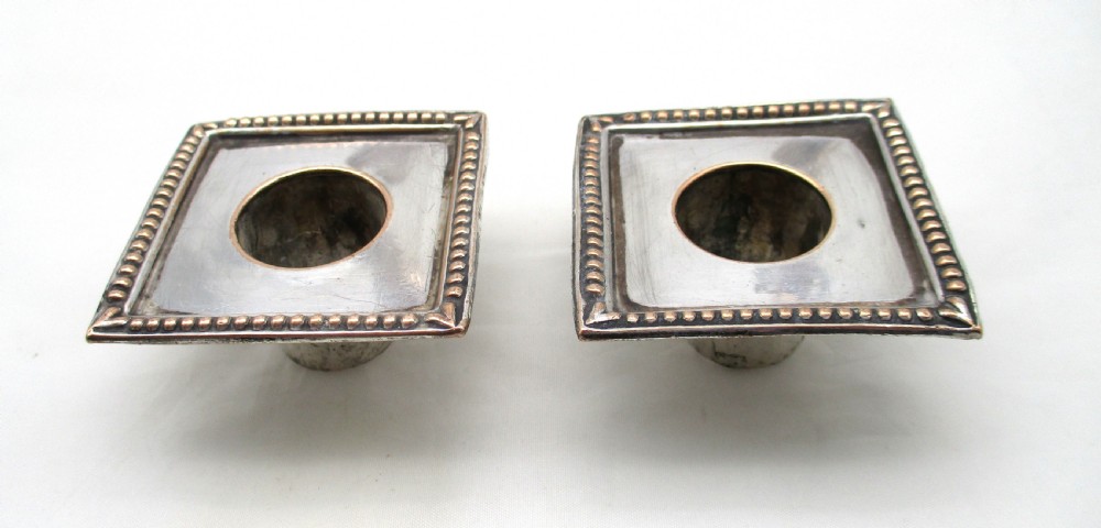 A pair of 18th-century Old Sheffield plated silver candlesticks featuring fluted columns, beaded square bases, and square nozzles. View X