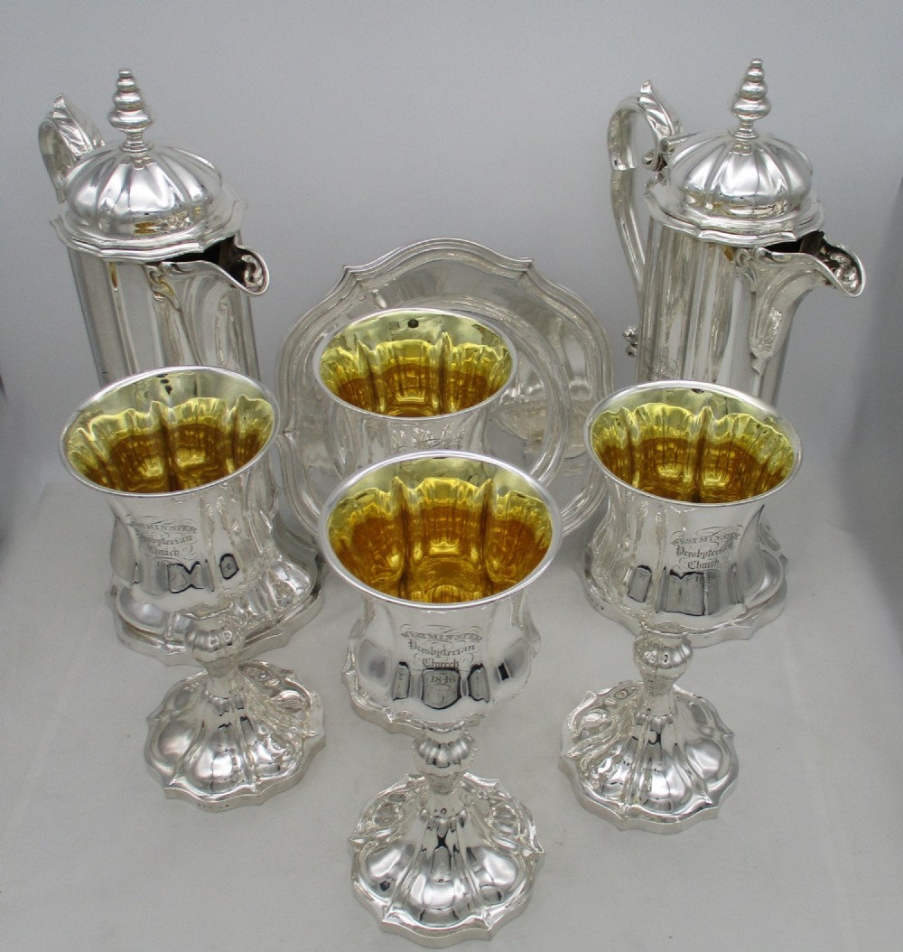 A seven-piece silver-plated Victorian communion set featuring two tall lidded flagons, four chalices with gilded interiors, and a shaped waiter tray with church inscriptions.