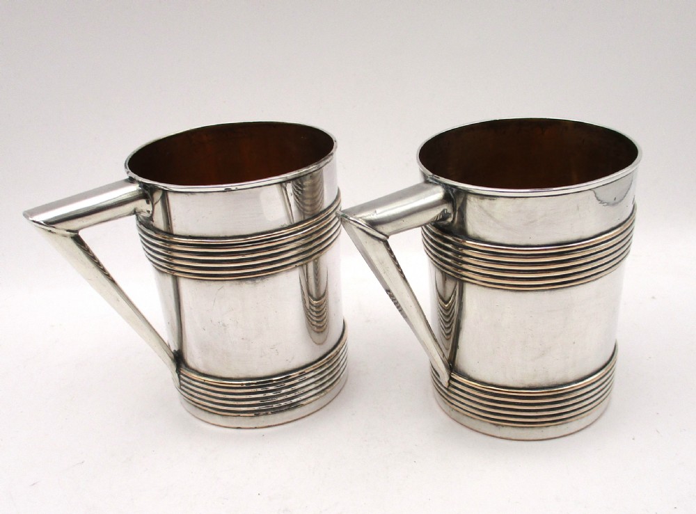 A pair of cylindrical silver-plated tankards featuring horizontal reeded bands, angular handles, and gilded interiors. View III