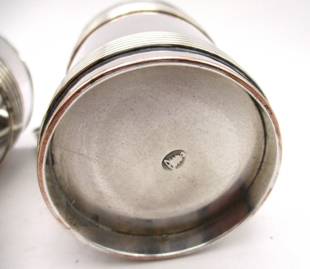 A pair of cylindrical silver-plated tankards featuring horizontal reeded bands, angular handles, and gilded interiors. View V