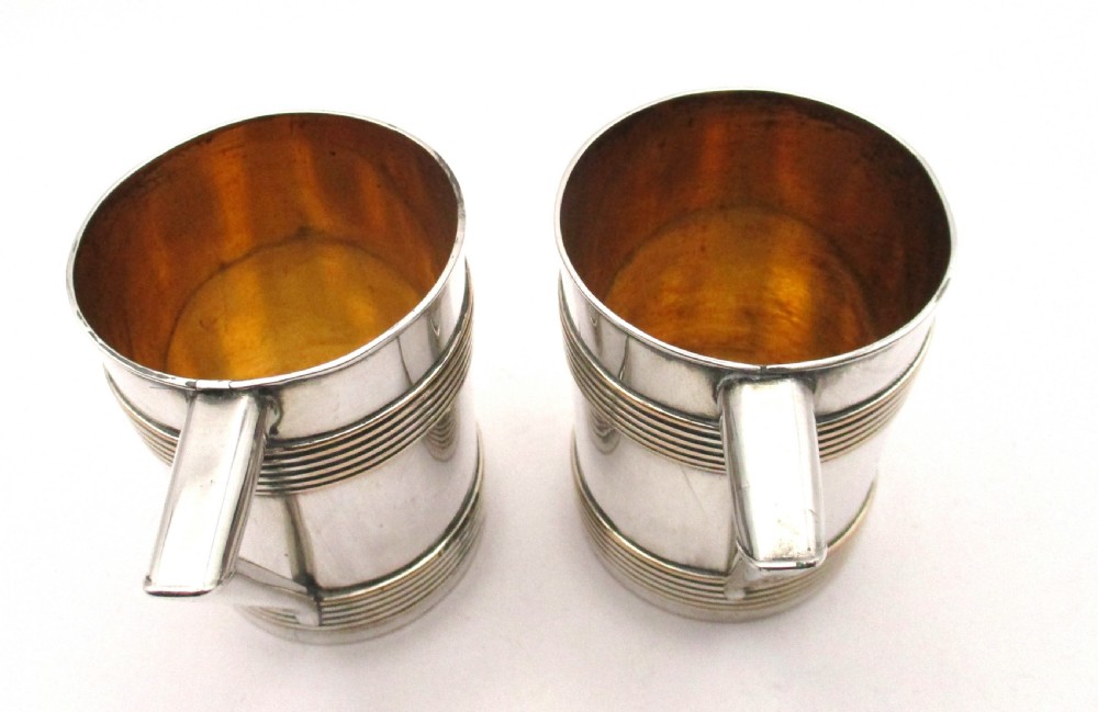 A pair of cylindrical silver-plated tankards featuring horizontal reeded bands, angular handles, and gilded interiors. View VI