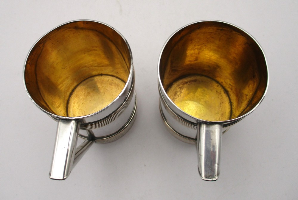 A pair of cylindrical silver-plated tankards featuring horizontal reeded bands, angular handles, and gilded interiors. View VII