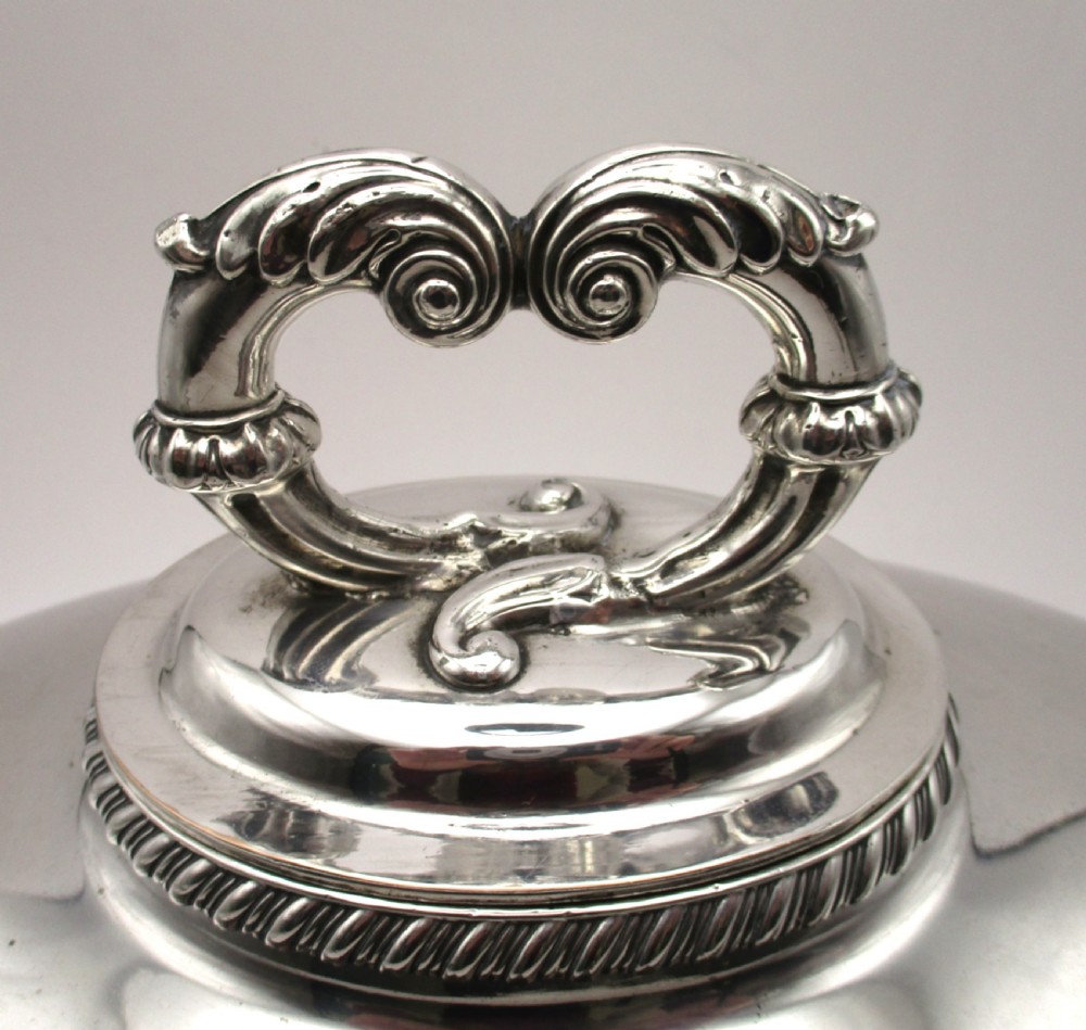 An oval domed silver-plated food cover featuring a cast leaf motif top handle and an engraved crest on the front. View II