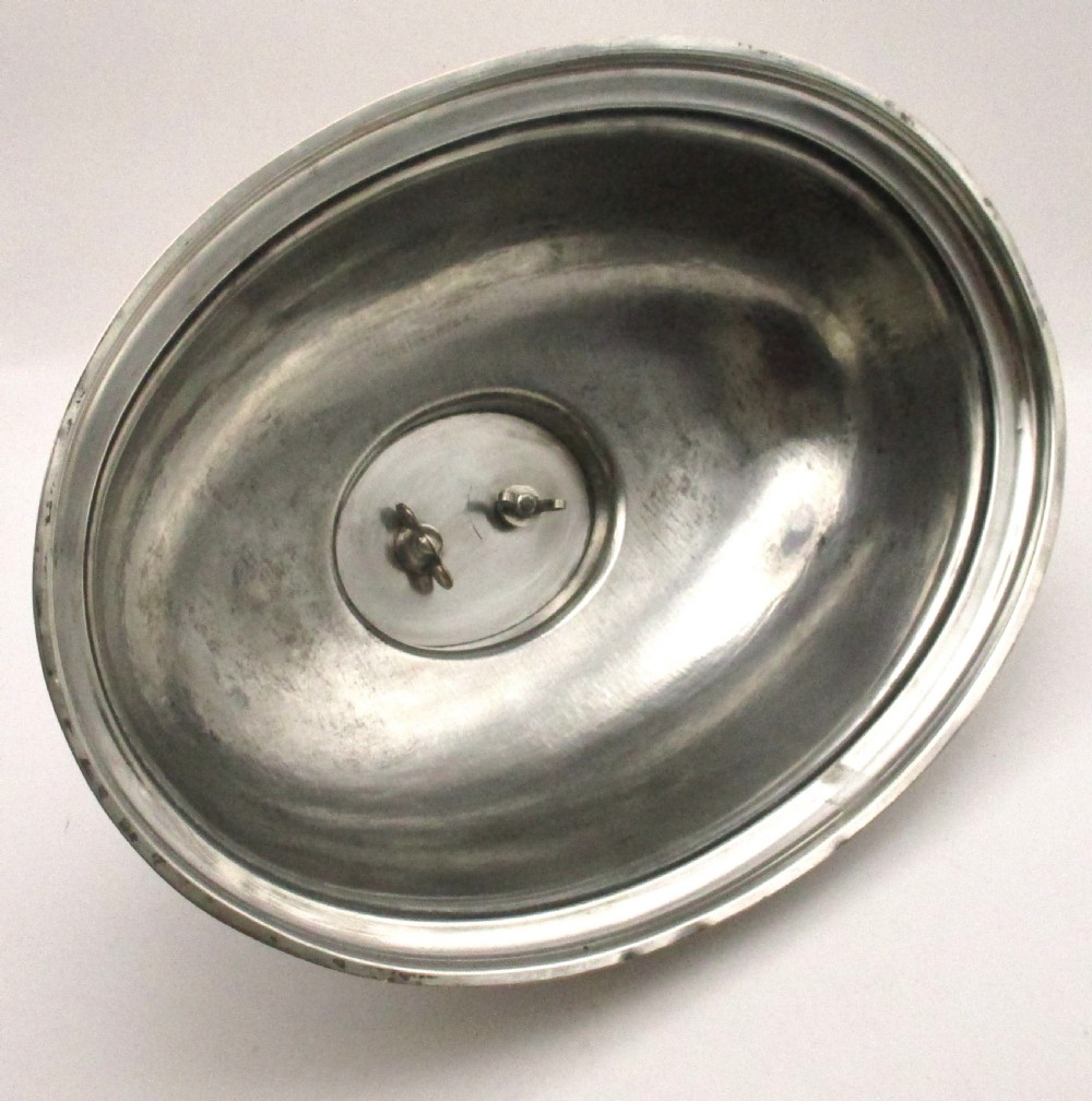 An oval domed silver-plated food cover featuring a cast leaf motif top handle and an engraved crest on the front. View IV