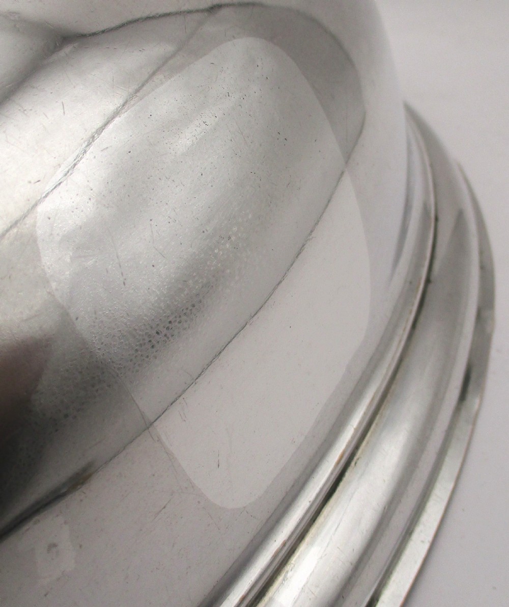 An oval domed silver-plated food cover featuring a cast leaf motif top handle and an engraved crest on the front. View VI