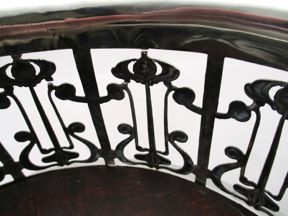 A circular Art Nouveau silver-plated coaster featuring openwork pierced floral fretwork around the gallery and a polished dark wood base resting on four small ball feet. View X