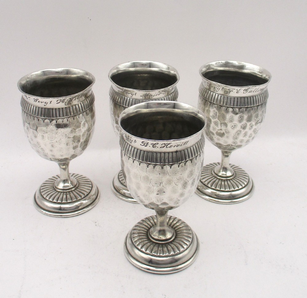 A set of four silver-plated goblets with engraved military ranks, hammered bodies, and reeded base rims.
